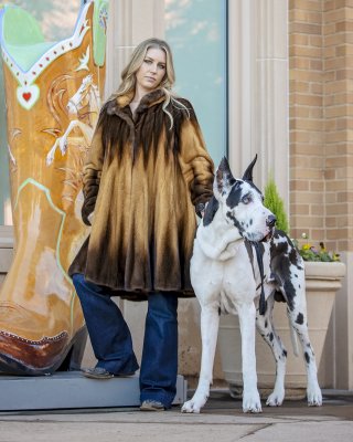 woamns with a Great Dane wearing a fur coat standing next to a boot sculpture